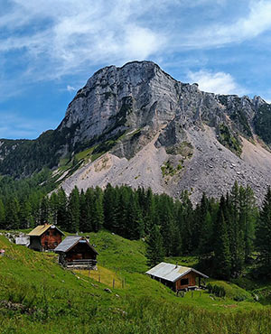 Mehrere Alm-Hütten stehen auf einem hügeligen Gelände in den österreichischen Alpen