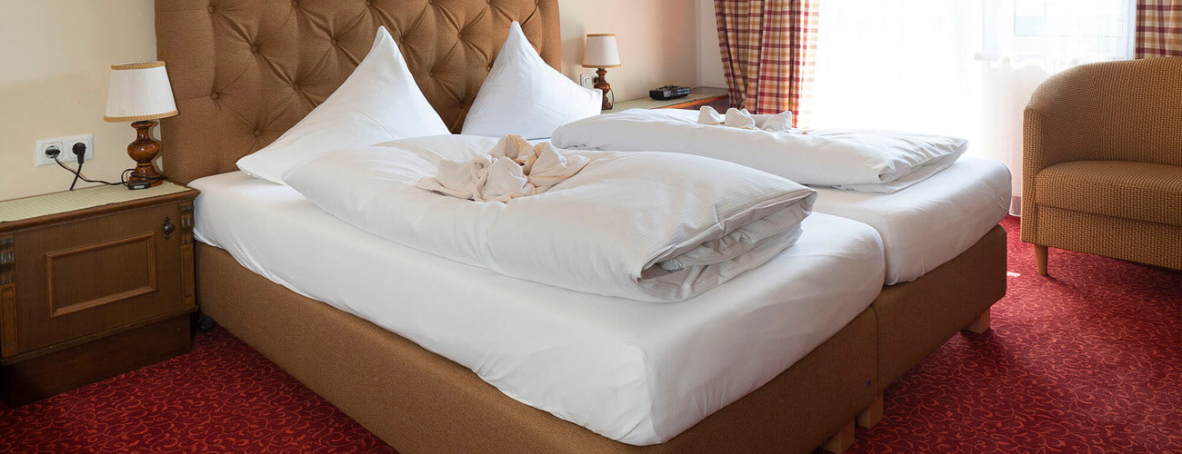 Ein Doppelbett mit weißem Bettlaken und weißer Bettwäsche steht auf einem roten Teppichboden